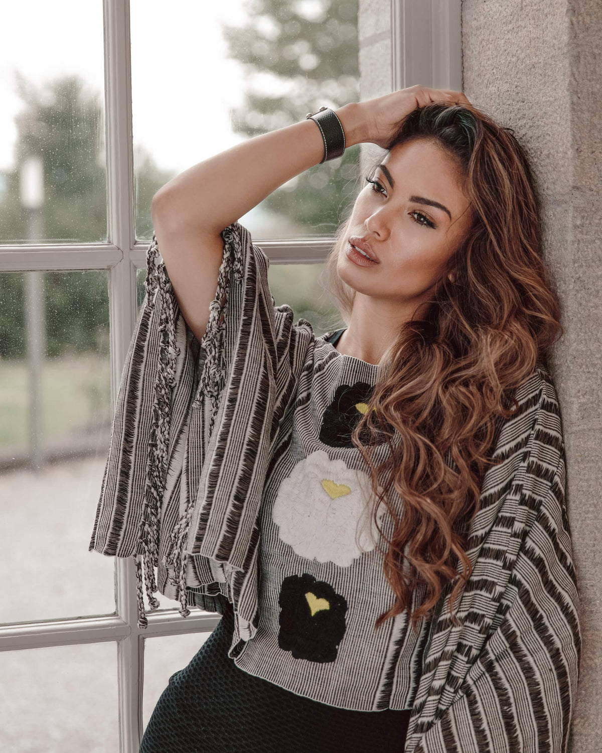 Serene woman leaning next to a window wearing Táabal flowers poncho by 32 Estados
